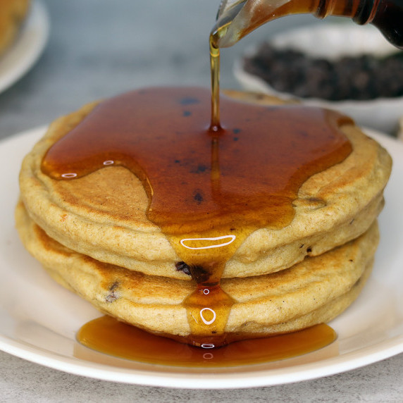 Stack of chocolate chip ricotta pancakes on a white plate with syrup pouring over them.