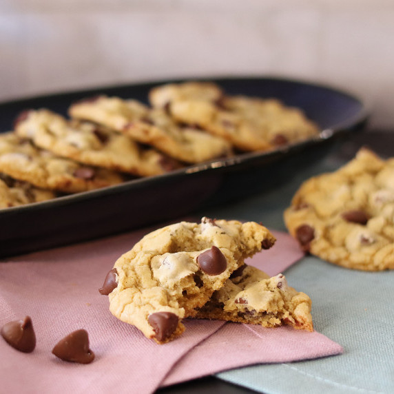 A broken chocolate chipper champ cookie on a napkin, more cookies in the background