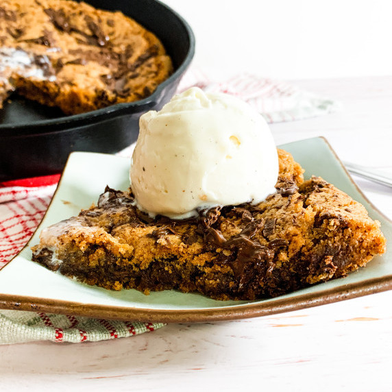 wedge of gooey chocolate chunk skillet cookie with a scoop of melty vanilla ice cream on top