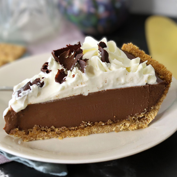 A slice of chocolate cream pie on a white plate with a gold pie server to the right.