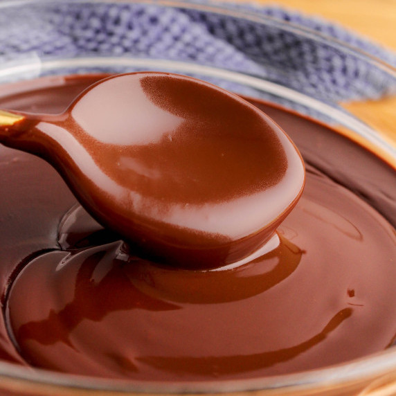 Chocolate ganache in clear glass bowl with gold spoon on wood table with blue tea-towel