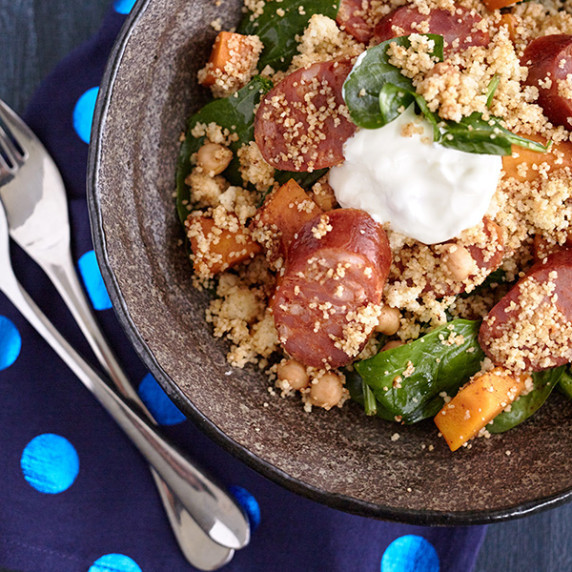 Sliced Chorizo sausage with cubed pumpkin, couscous, spinach, and chickpeas, garnished with a dollop