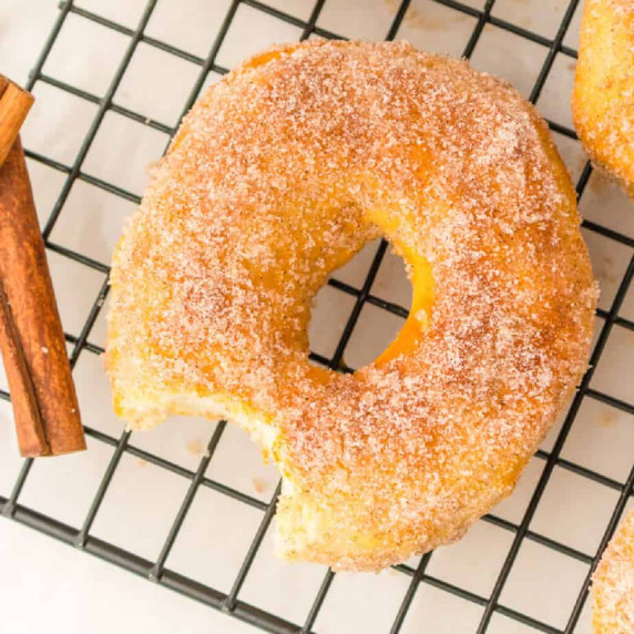 Close up overhead of a cinnamon sugar coated donut with a bite missing cooling on a wire rack.