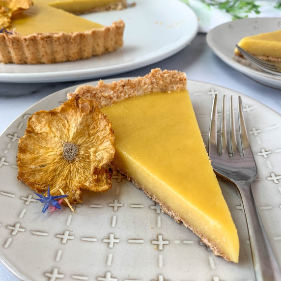 Slice of coconut pineapple tart on a white plate with a pineapple flower next to it