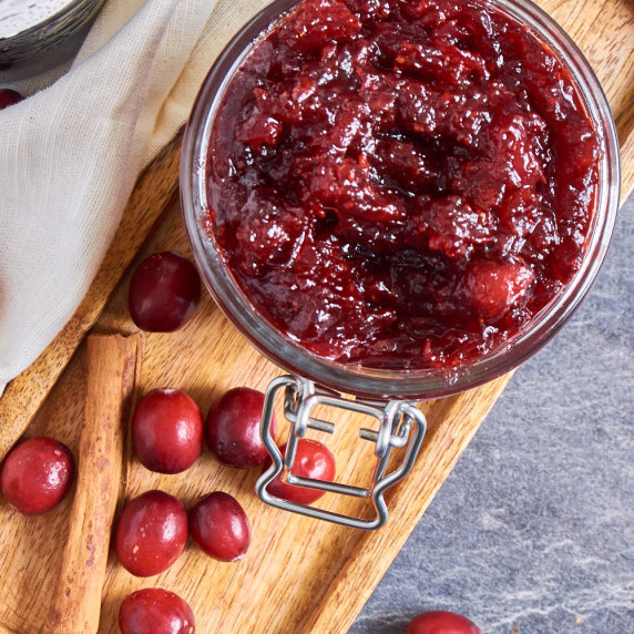 A jar of Cranberry Sauce with Port and Clementines surrounded by fresh cranberries and cinnamon