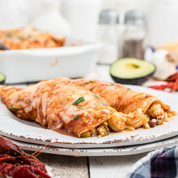 two crawfish enchiladas on a plate with some crawfish falling out.