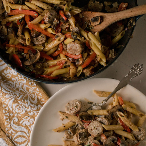 a pan and plate with a creamy pasta dish with sausage, red peppers and herbs 