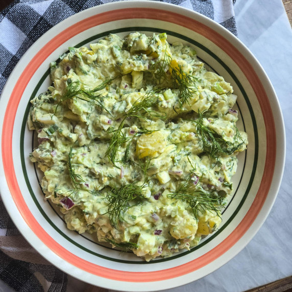 A pink rimmed bowl full of creamy potato salad with pops of green dill.