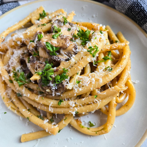 A golden nest of pasta with pops of white and green on a white plate.