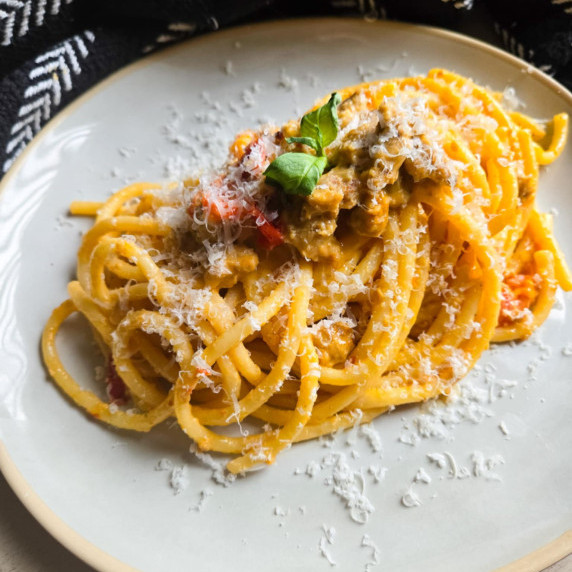 A golden nest of bucatini pasta topped with green basil against a black towel background.