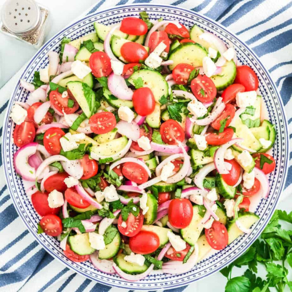Cucumber tomato salad in a large serving bowl from overhead with a napkin with blue & white stripes