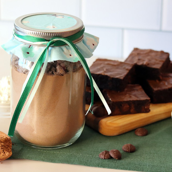 A jar of the DIY brownie mix in front of a board with baked brownies on it.