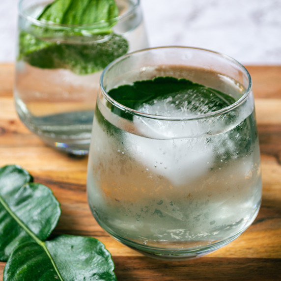 Photo of a yuzu mocktial in a glass with kaffir lime leaves in the foreground. 
