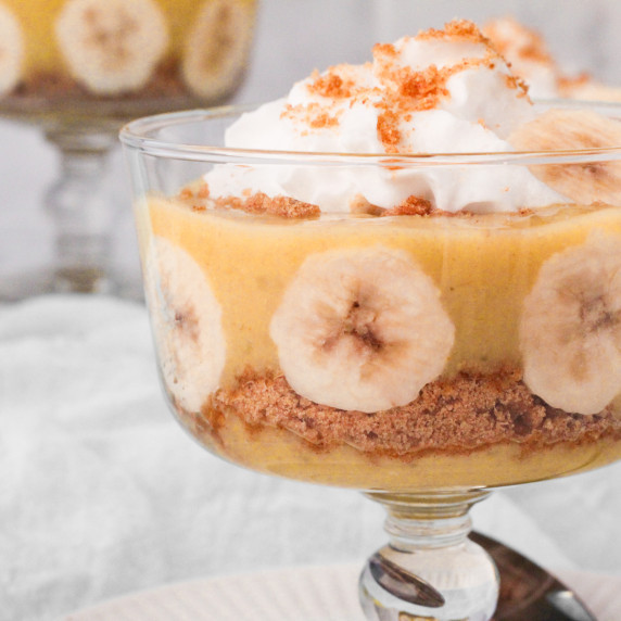 A glass dish with banana pudding layered with cookie crumbs and banana slices topped with cream.