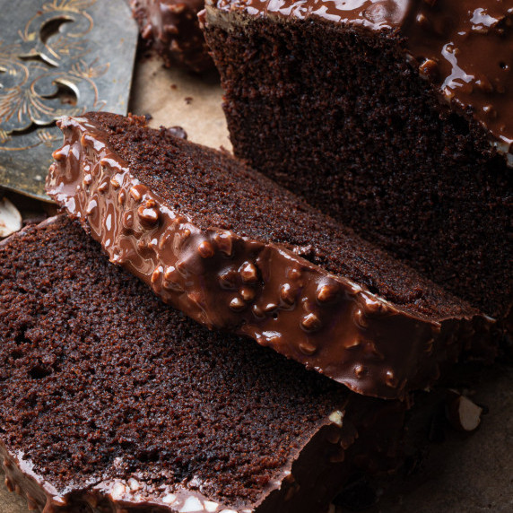 slices of chocolate loaf cake with chocolate almond glaze on parchment paper with a cake server