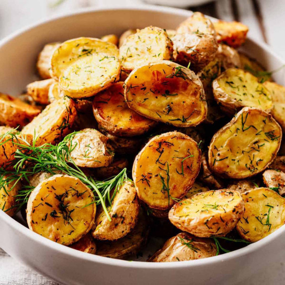 Crispy roasted baby potatoes with fresh dill, served in a white bowl.
