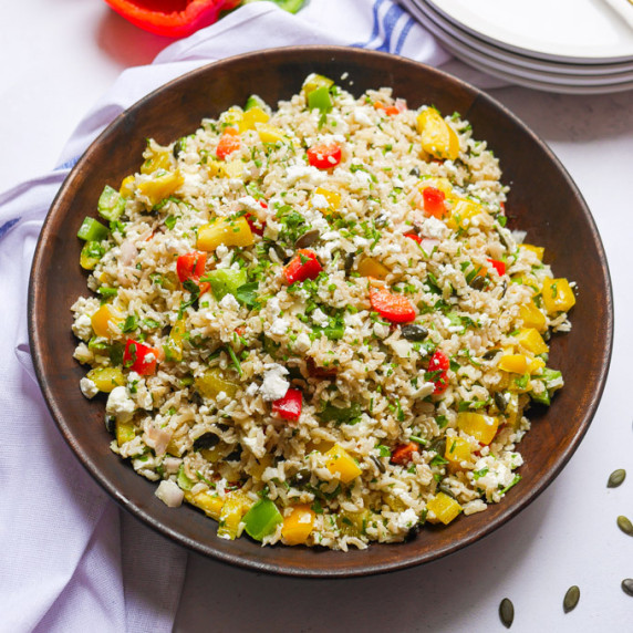 Bell pepper and brow rice salad in a wooden bowl, garnished with feta and parsley