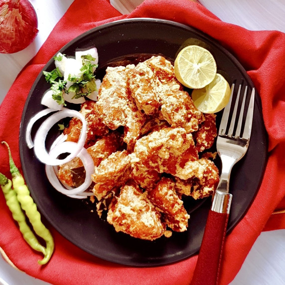 Indian fried chicken on a black plate placed over a red cloth with a fork on the side.