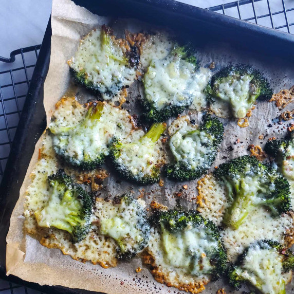 A parchment lined tray of smashed, green broccoli with white, melty cheese.