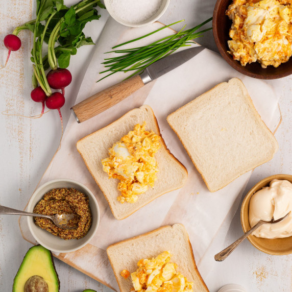 Slices of bread on a wooden board with egg sandwich filling ready to spread out