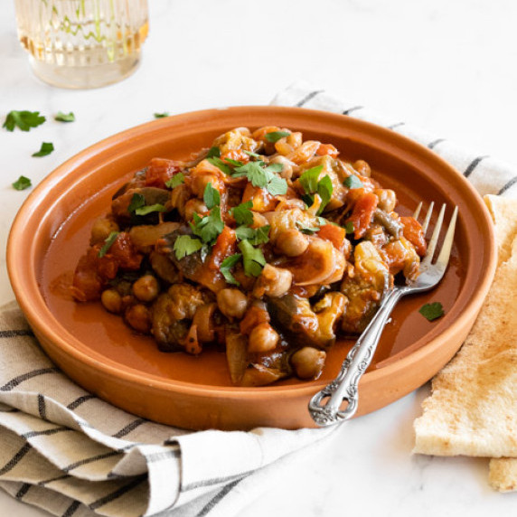 lebanese eggplant moussaka on a terracotta plate with a fork and pita bread on the side.