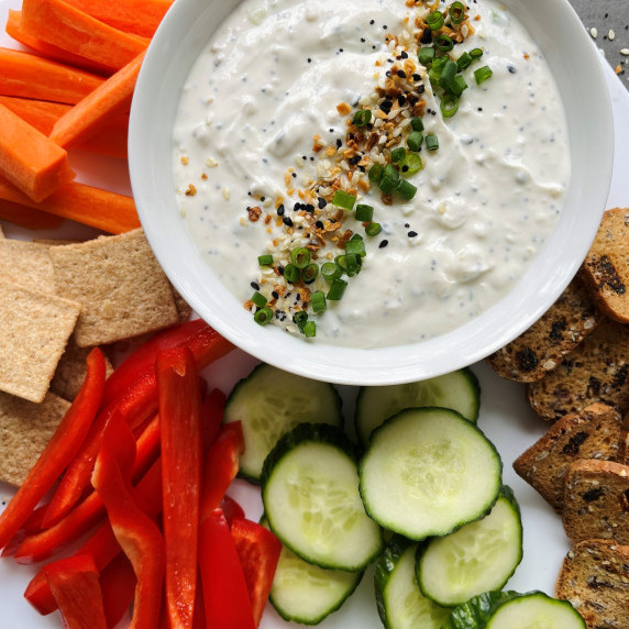 Onion dip in a white bowl surrounded by cucumber slices, red pepper strips, carrots and crackers.