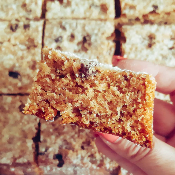 Hand holding a slice of Greek Fanouropita, a spiced olive-oil cake with orange and cinnamon.