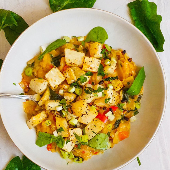 celeriac with other veggies and greens in a white bowl on a marbled background with spinach leaves