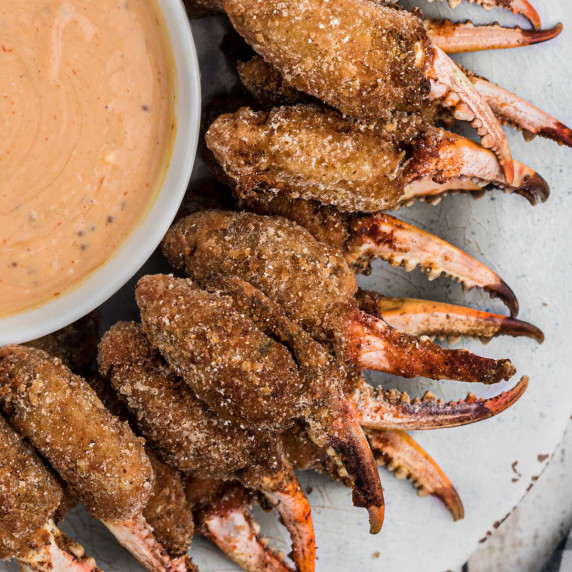 a plate full of fried crab claws with a bowl of dip in the back