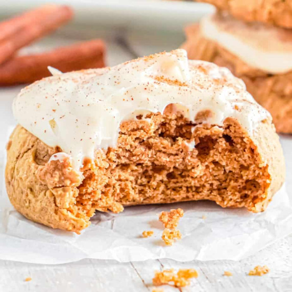 Up close view of a pumpkin cookie with frosting with a bite missing.