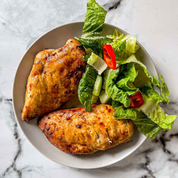 A closeup of chicken breasts on a white plate with salad.