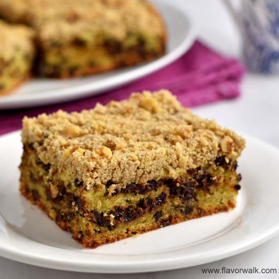 A slice of gluten free crumb cake on a small white plate with more cake in the background.