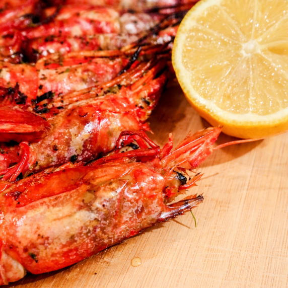 Sautéed garlic shrimp served with a lemon wedge on a wooden board.