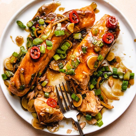 Salmon with soy ginger glaze, scallions and garlic on a white plate with steel fork