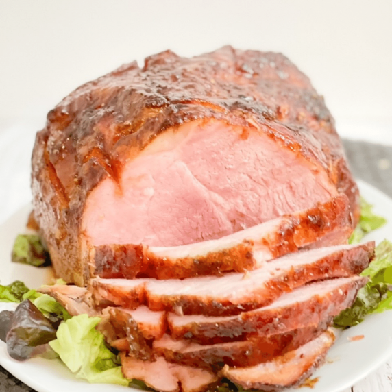 A double smoked ham on a white platter with thin slices off the front.