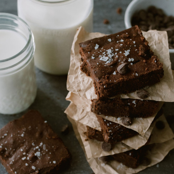 healthy gluten free fudgy buckwheat brownies arranged in a pile beside a tall glass of milk 