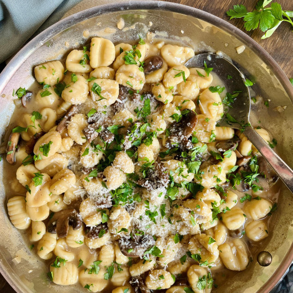 Skillet filled with gnocchi and mushrooms in a cream sauce topped with parsley and grated cheese.