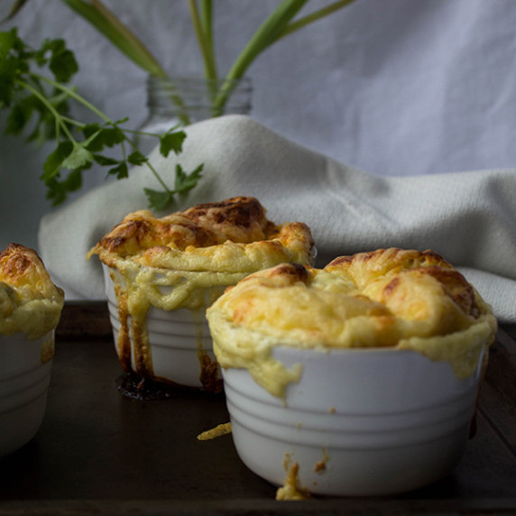 Two goat cheese souffles in white ramekins on a baking sheet