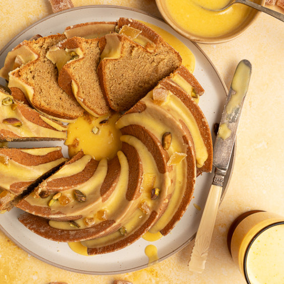 A bundt cake on a plate cut into pieces and surrounded by plates