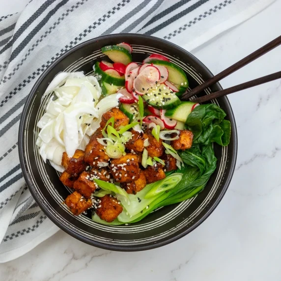 A vibrant gochujang tofu rice bowl served in a black bowl with chopsticks.
