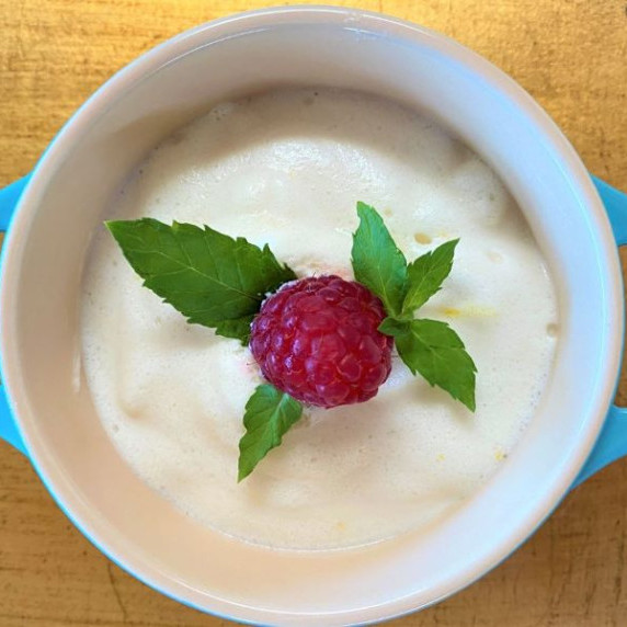 Single serving of light colored lemon mousse garnished with raspberry in the center and mint leaves 
