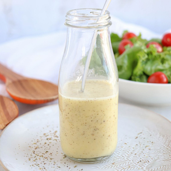 a glass bottle with homemade Greek salad dressing on a plate and a green salad in the background