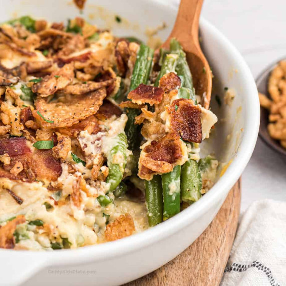 Close up of spoon scooping green bean casserole with bacon from a casserole dish.