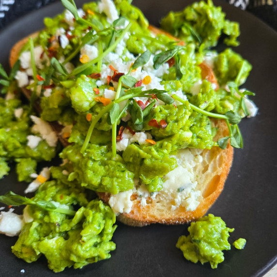 A golden piece of toast topped with green eggs and shoots on a black plate.