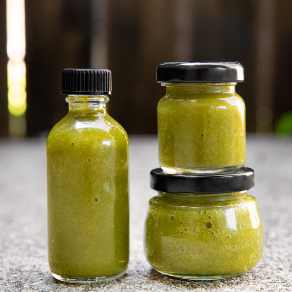 Three little glass bottles of green hot sauce.