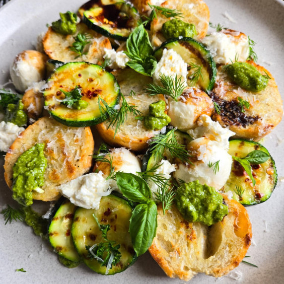 Pops of brown and contrasting green herbs, cheese, and bread on a white plate.