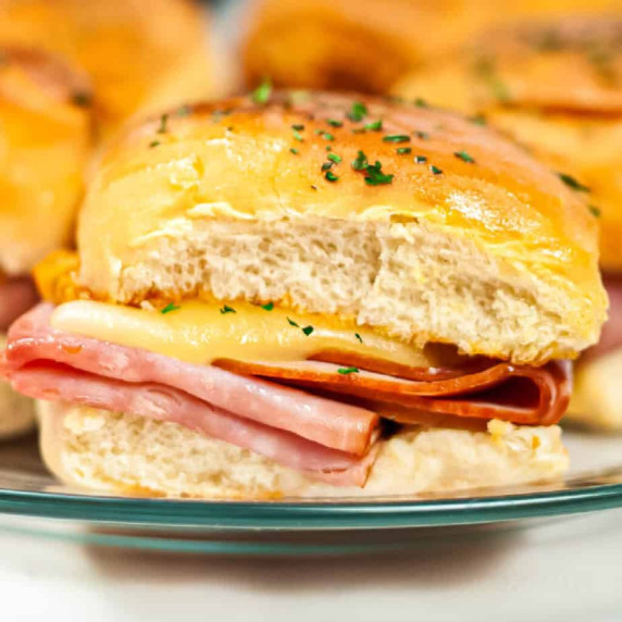 Melty ham and cheese slider up close on a plate from the side.