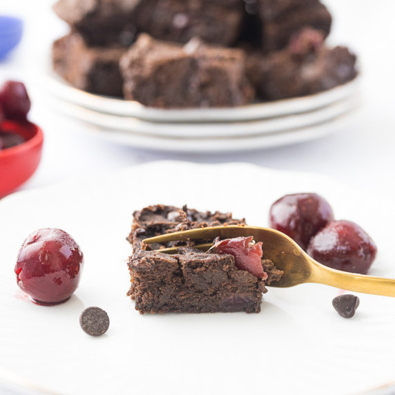Fudgy Cherry Chocolate Protein Brownie on white plate with gold fork taking a scoop