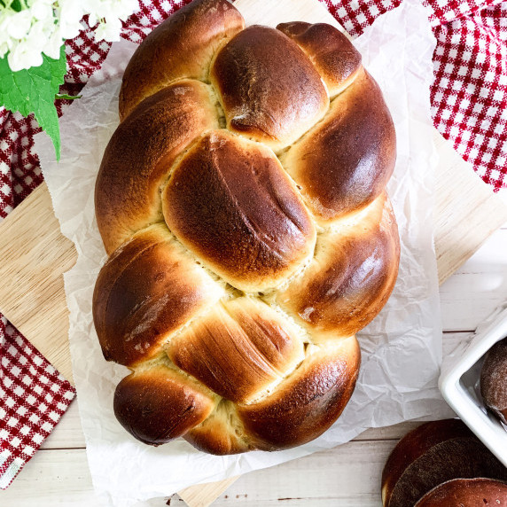 braided honey brioche on parchment lined wood cutting board over red gingham cloth