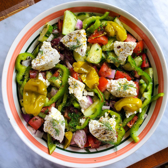 A colourful array of fresh produce & white feta cheese in a pink rimmed bowl against marble.